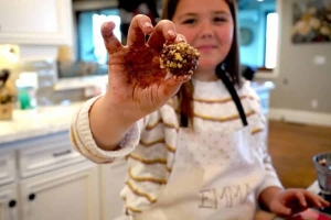 A young girl holds up a Chocolate Walnut Truffle up to show the camera.