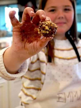 A young girl holds up a Chocolate Walnut Truffle up to show the camera.