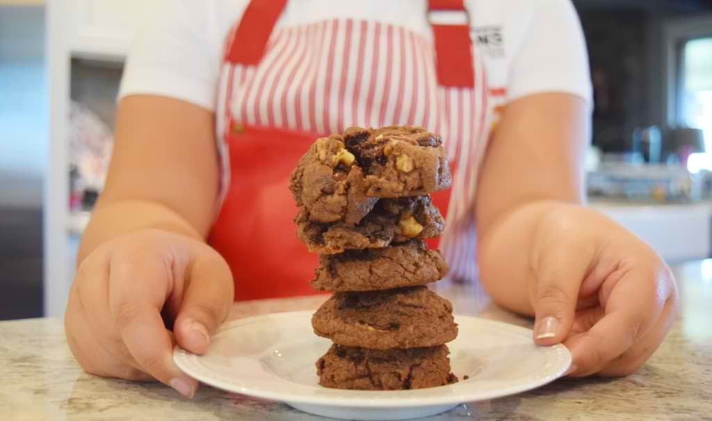 5 Chocolate cookies stacked up on a plate held by a young girl.