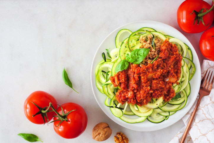 Healthy plant-based zucchini pasta topped with meatless walnut cauliflower bolognese, top view table scene on a white marble background