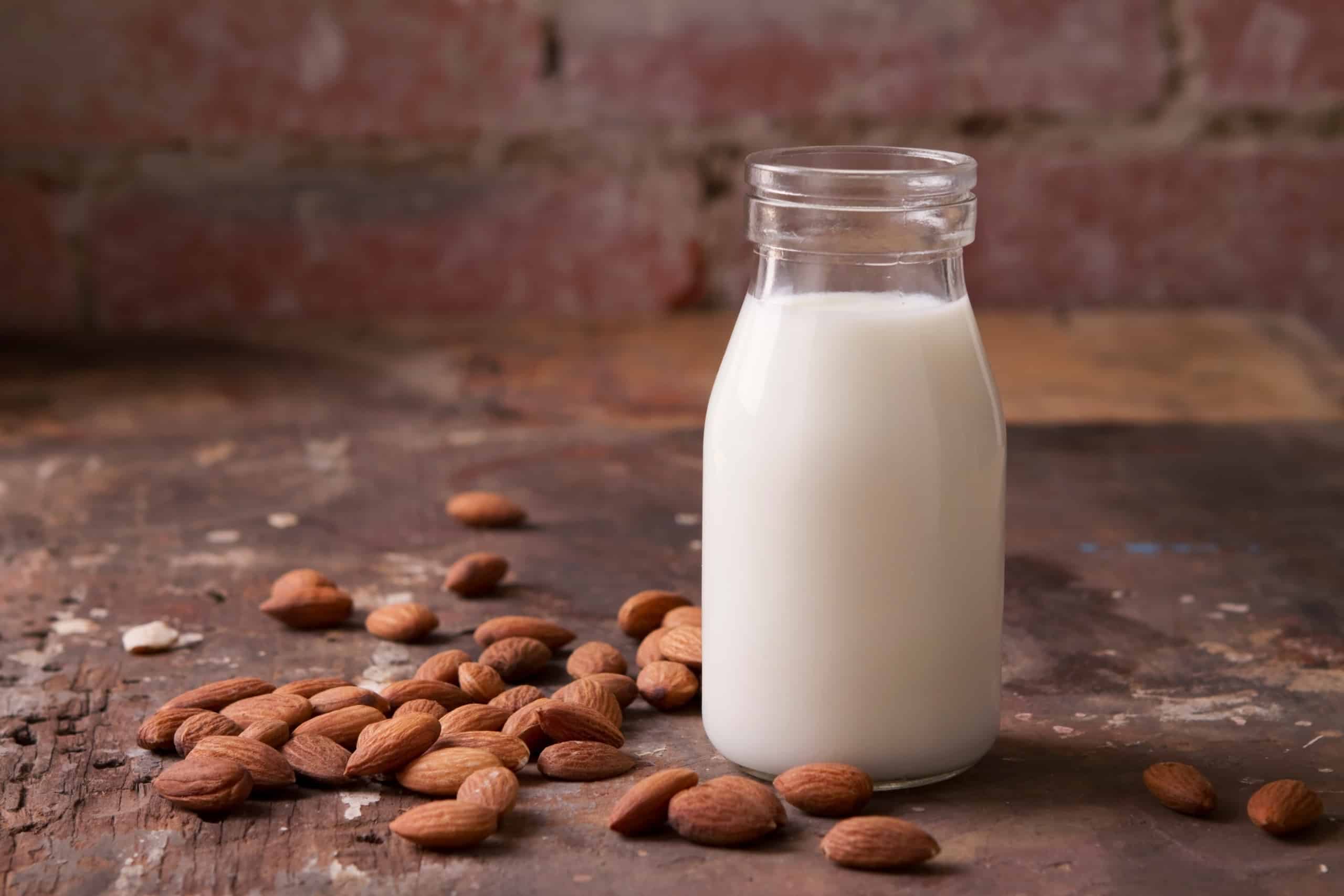 A jar of almond milk with almonds on the table near it.