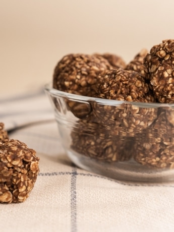 Almond butter energy bites in a clear bowl and on the white counter.