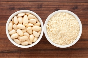 A bowl of almonds next to a bowl of almond flour