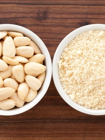 A bowl of almonds next to a bowl of almond flour