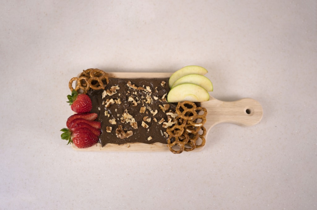 Butter Board with Cocoa Almond Butter, Organic Walnuts, green apple, and strawberries on a wooden serving board.